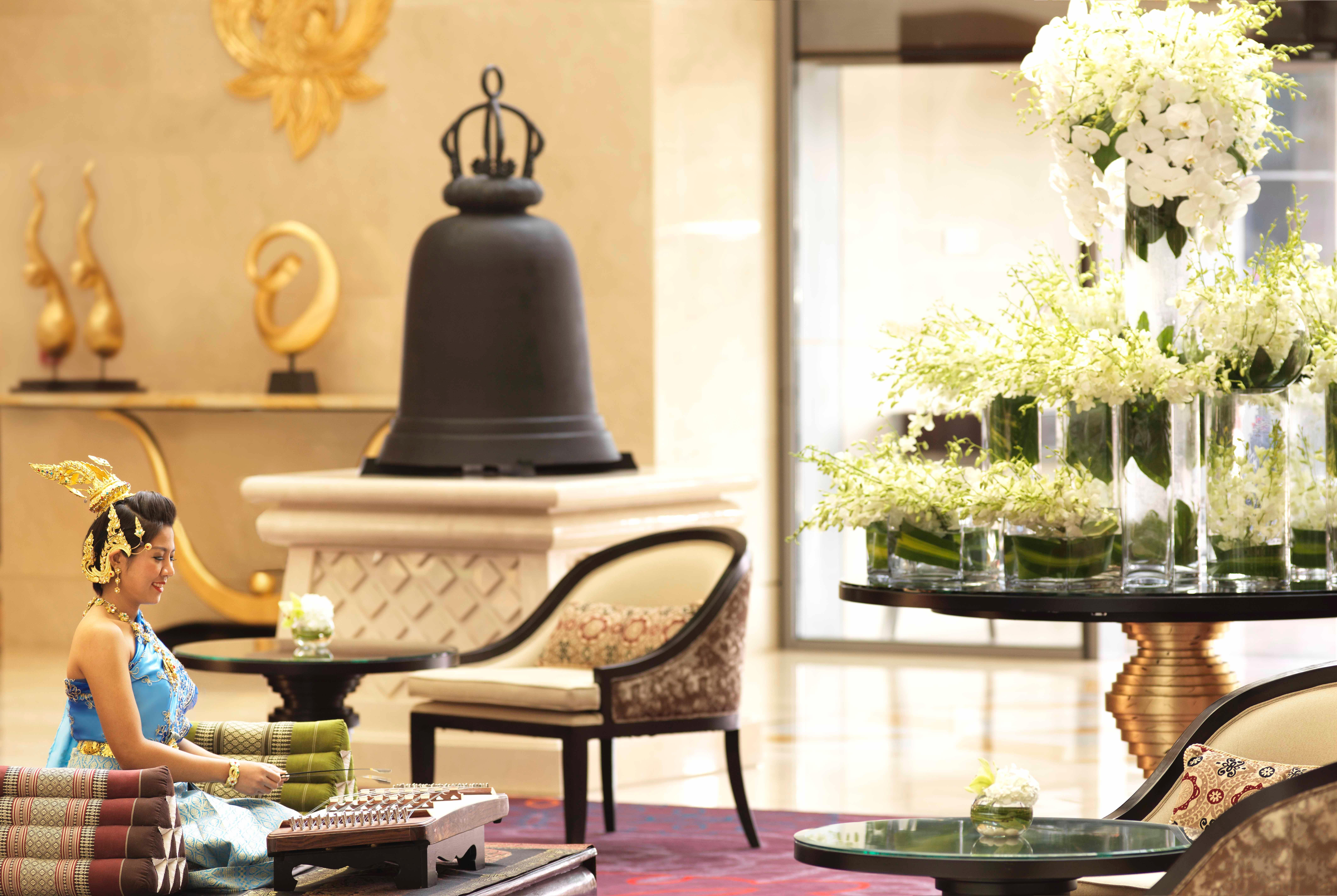 Dusit Thani Abu Dhabi Exterior photo The photo depicts an elegant lobby setting. In the foreground, a woman is seated on a chair, surrounded by neatly arranged colorful towels. She appears to be engaged in an activity or simply enjoying the ambiance. 

In the background, there is a larg