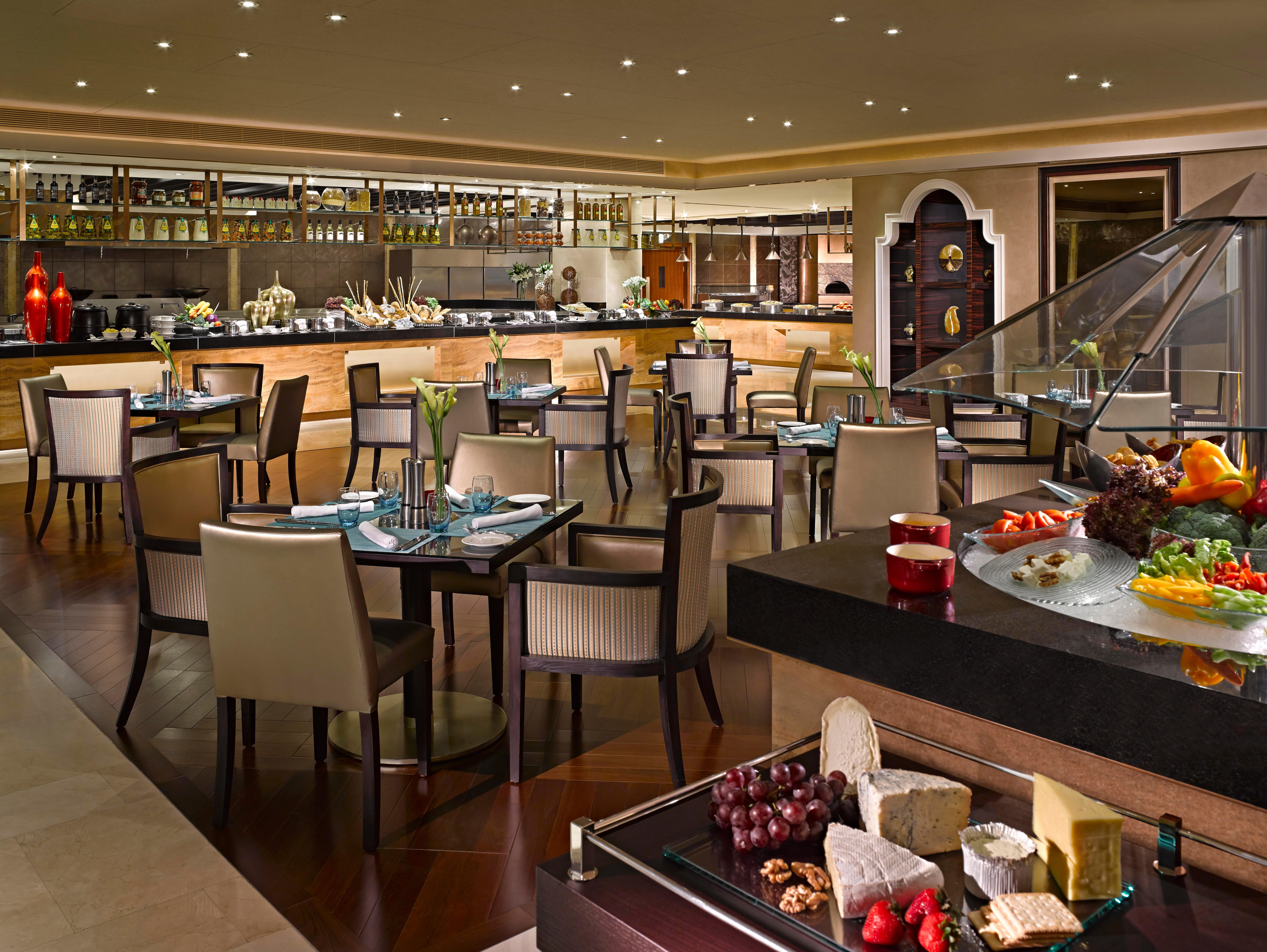 Dusit Thani Abu Dhabi Exterior photo The photo depicts a spacious and elegantly designed restaurant interior. It features a mix of wooden and modern furnishings, including numerous tables and chairs arranged throughout the dining area. On one side, there is a buffet setup with a variety