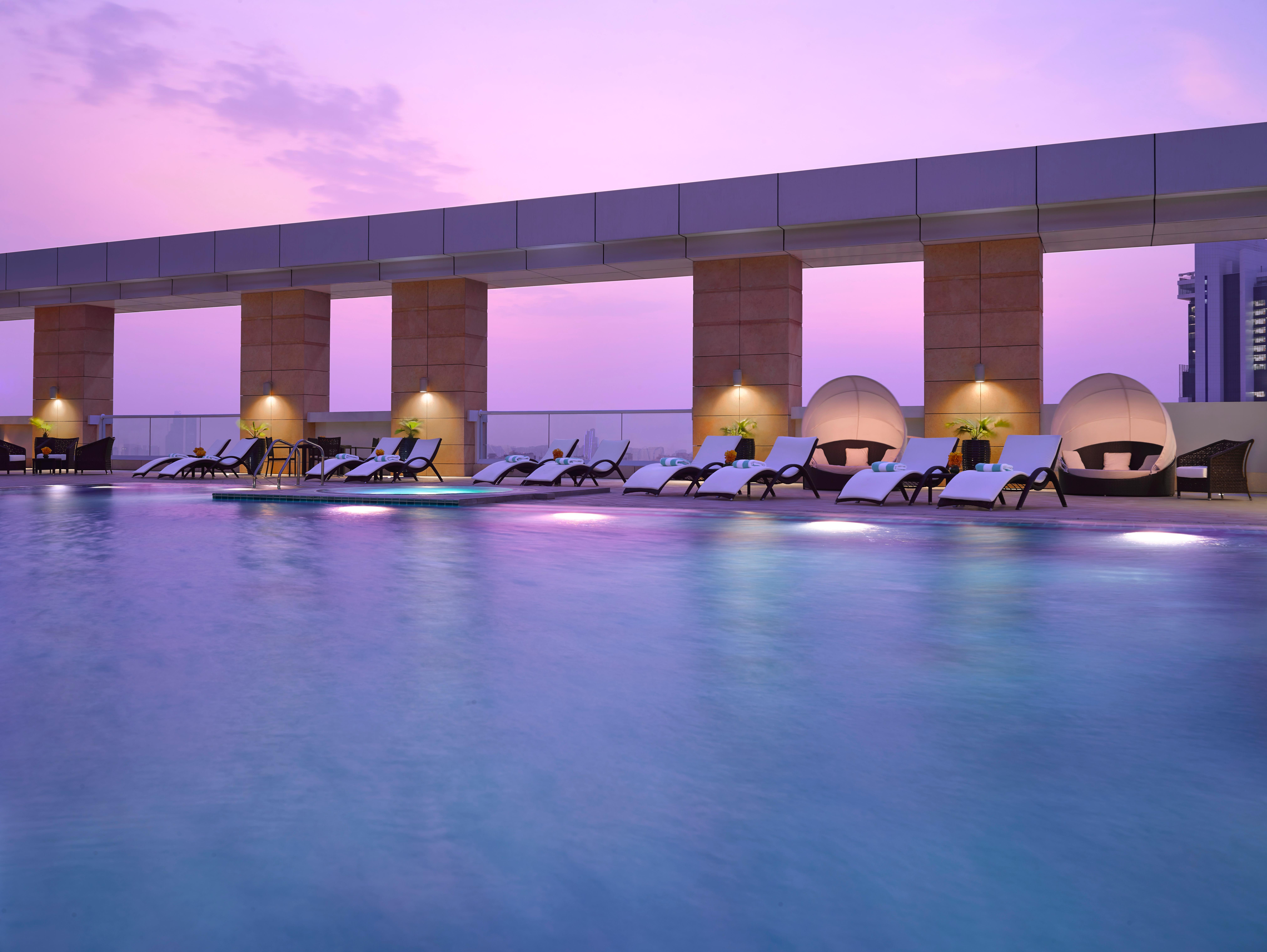 Dusit Thani Abu Dhabi Exterior photo The photo depicts a serene rooftop swimming pool area during twilight. The sky is illuminated with shades of purple, creating a calming atmosphere. Alongside the pool, there are several lounging chairs arranged neatly, along with modern circular caba