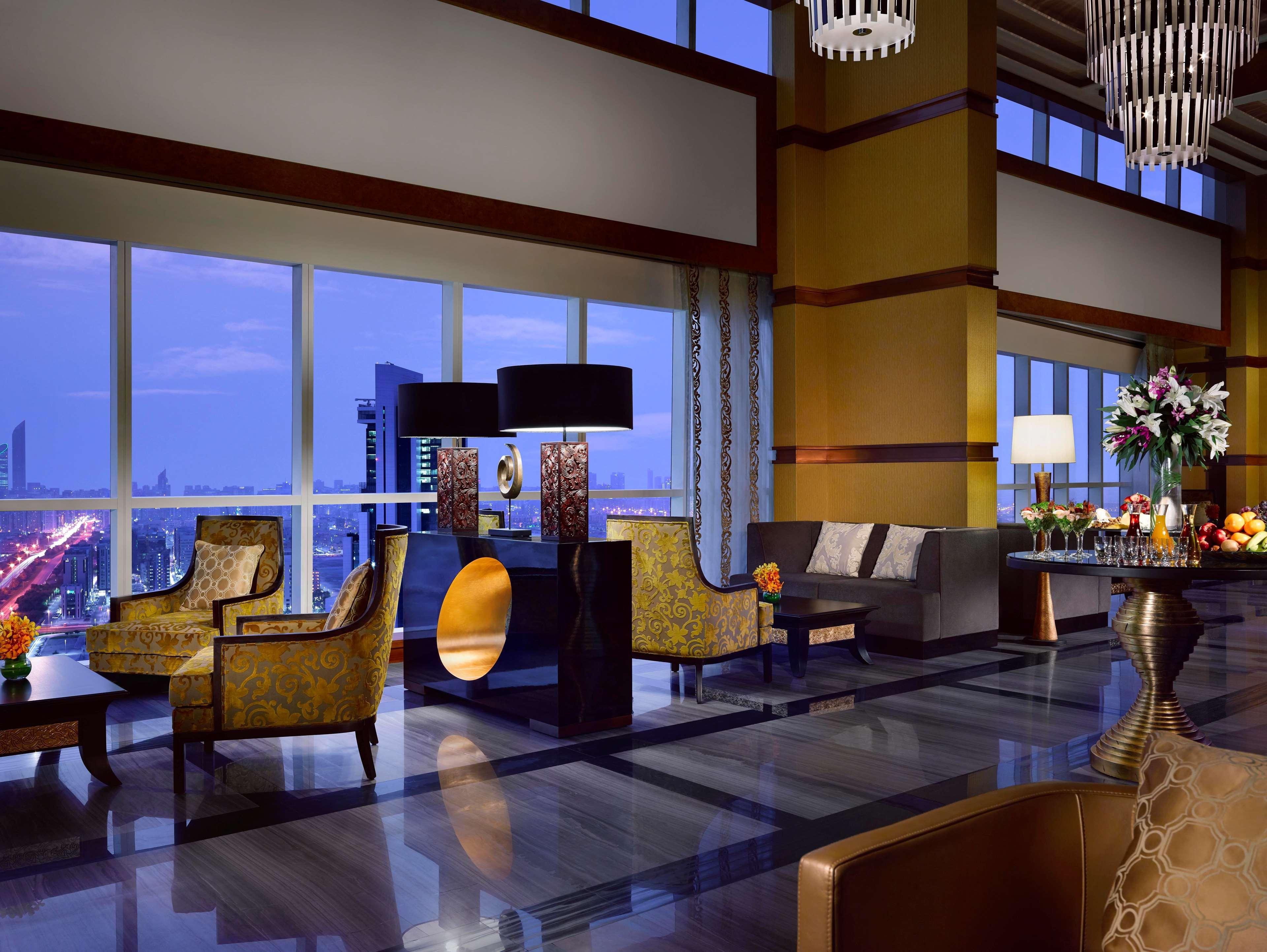 Dusit Thani Abu Dhabi Exterior photo The photo depicts a luxurious hotel lobby interior. It features elegant furniture, including stylish chairs and tables. Large windows allow natural light to fill the space, providing a view of the city skyline at twilight. The decor includes decorati