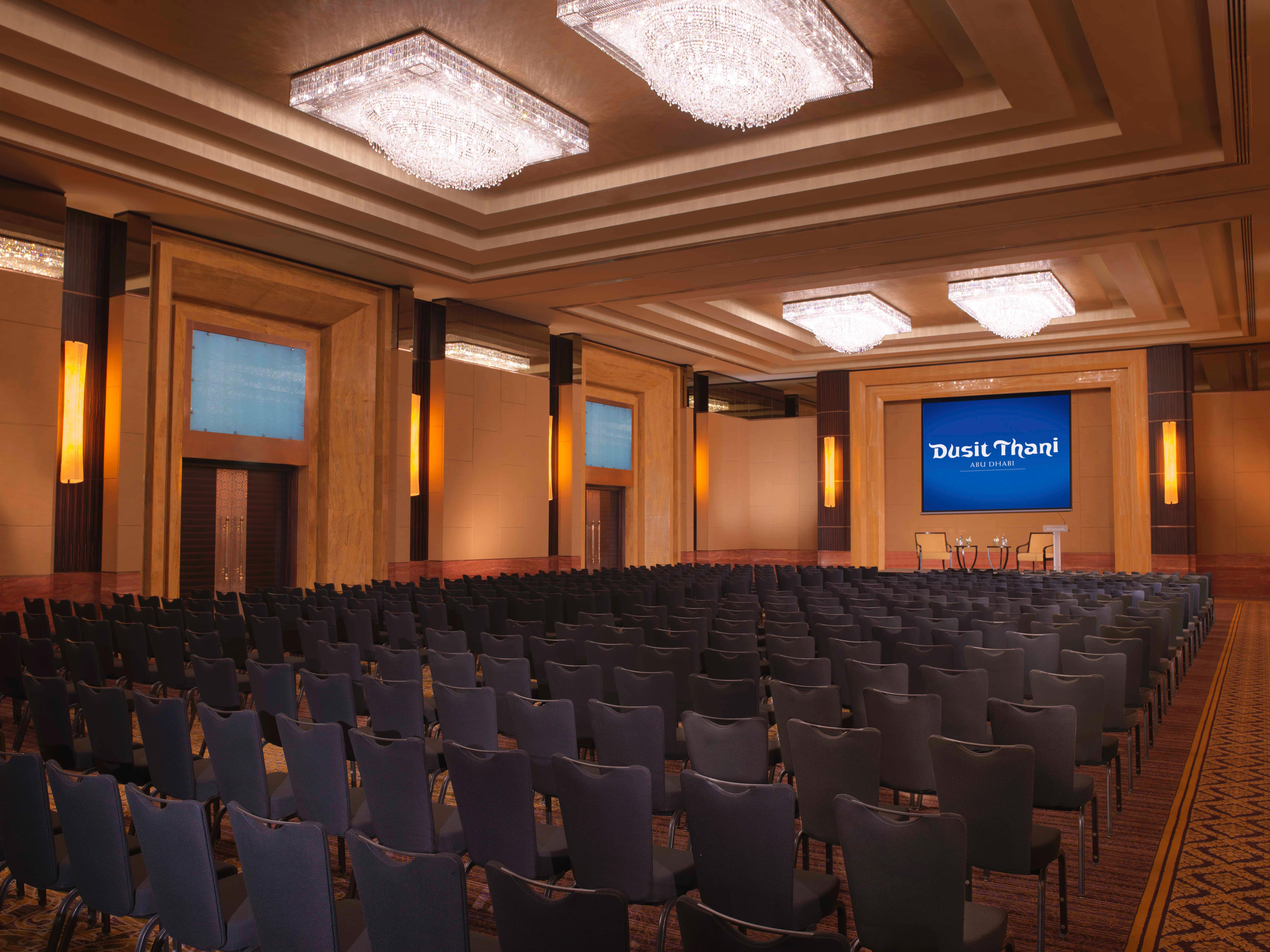 Dusit Thani Abu Dhabi Exterior photo The photo shows a well-lit auditorium or conference room set up for an event. The space features a large number of dark chairs arranged in rows facing a stage or presentation area. Above the stage, there is a screen displaying the text "Thank You!" i