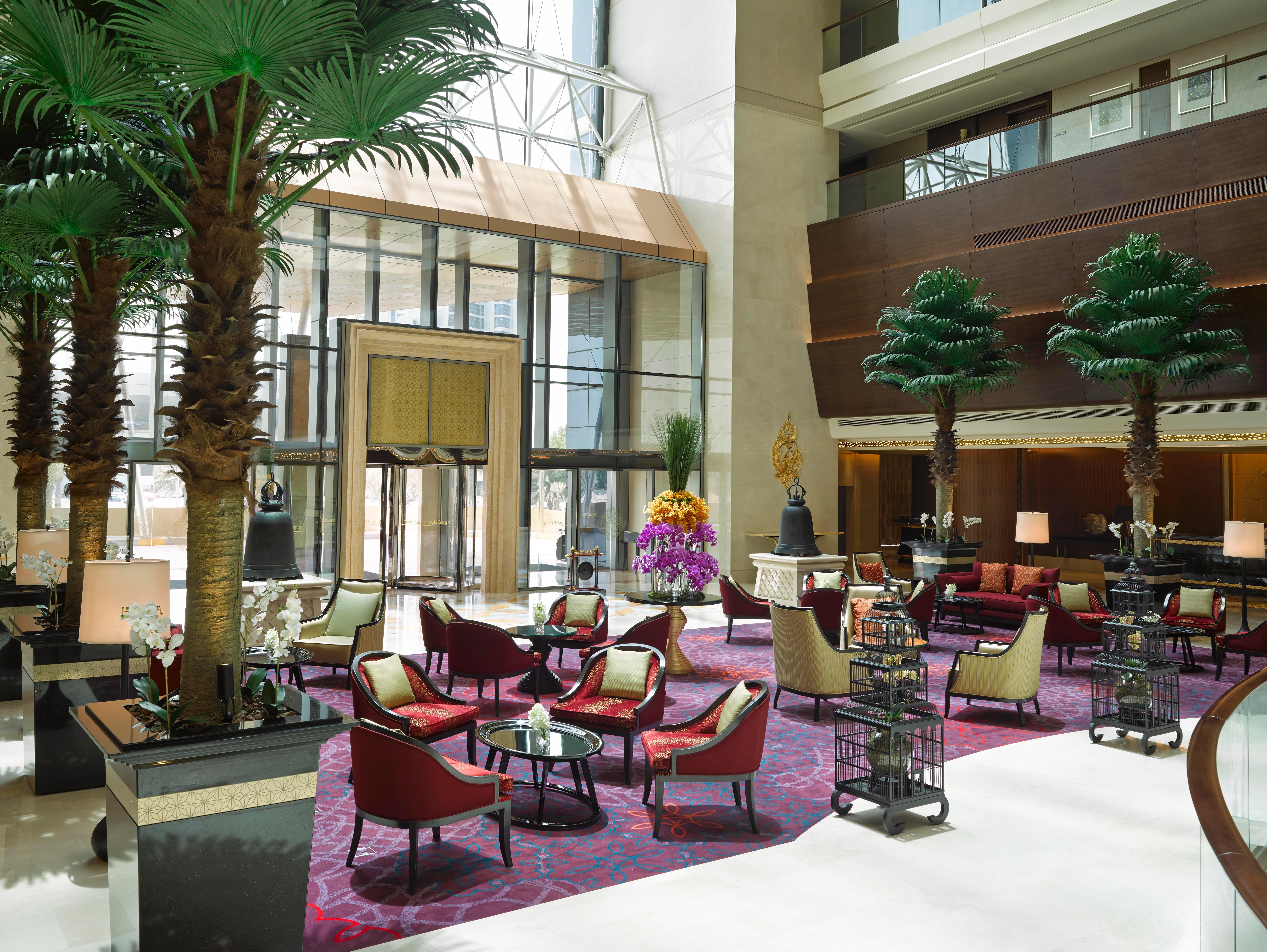 Dusit Thani Abu Dhabi Exterior photo The image shows a luxurious hotel lobby. It features tall palm trees that add a tropical touch, along with elegant seating areas consisting of comfortable armchairs and small tables. The decor includes rich colors, and the flooring has a plush carpet