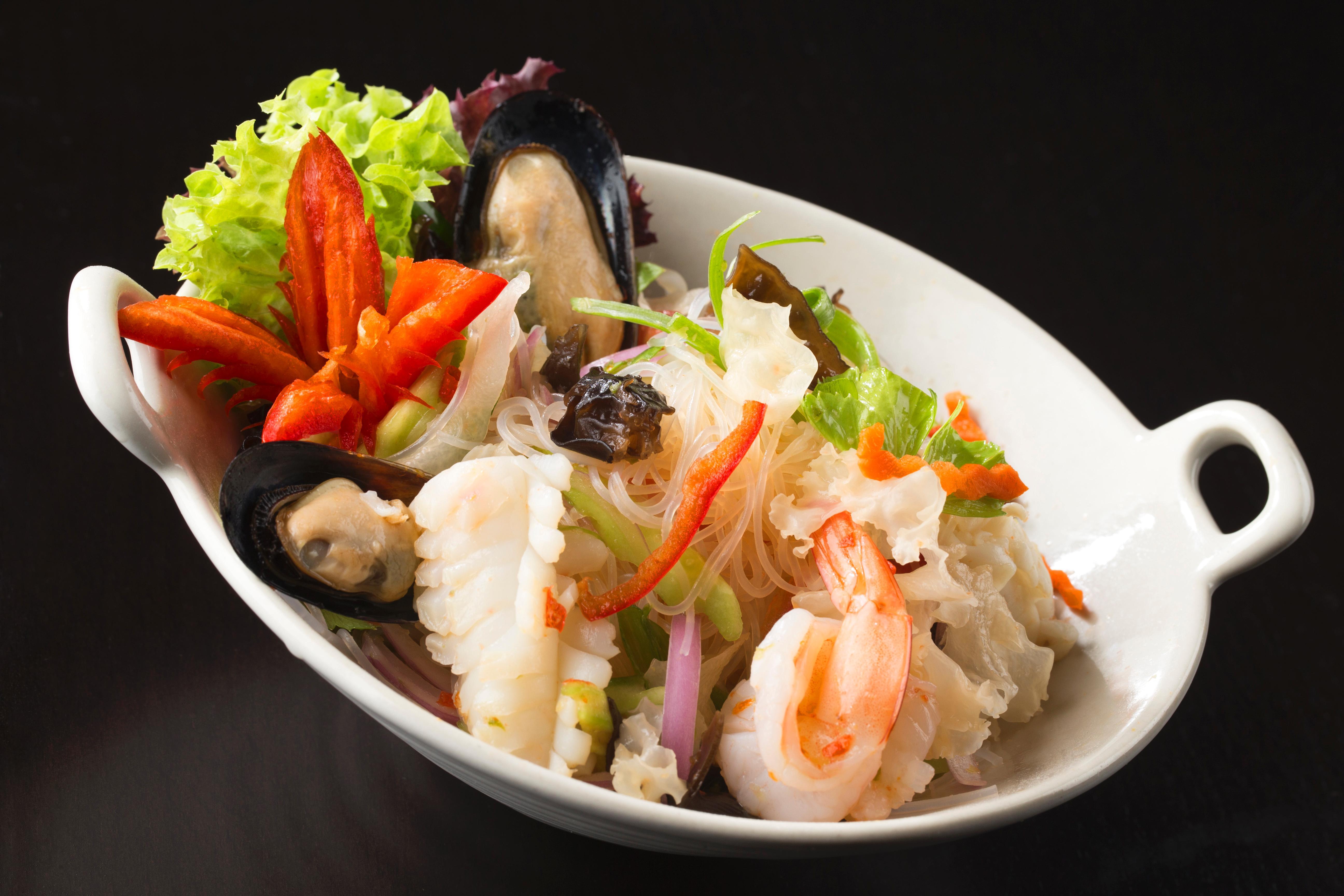 Dusit Thani Abu Dhabi Exterior photo The photo shows a beautifully arranged seafood salad served in a white dish. The salad contains a mix of ingredients, including shrimp, mussels, and various vegetables. There are bright green leaves of lettuce, slices of red chili peppers, and a medl