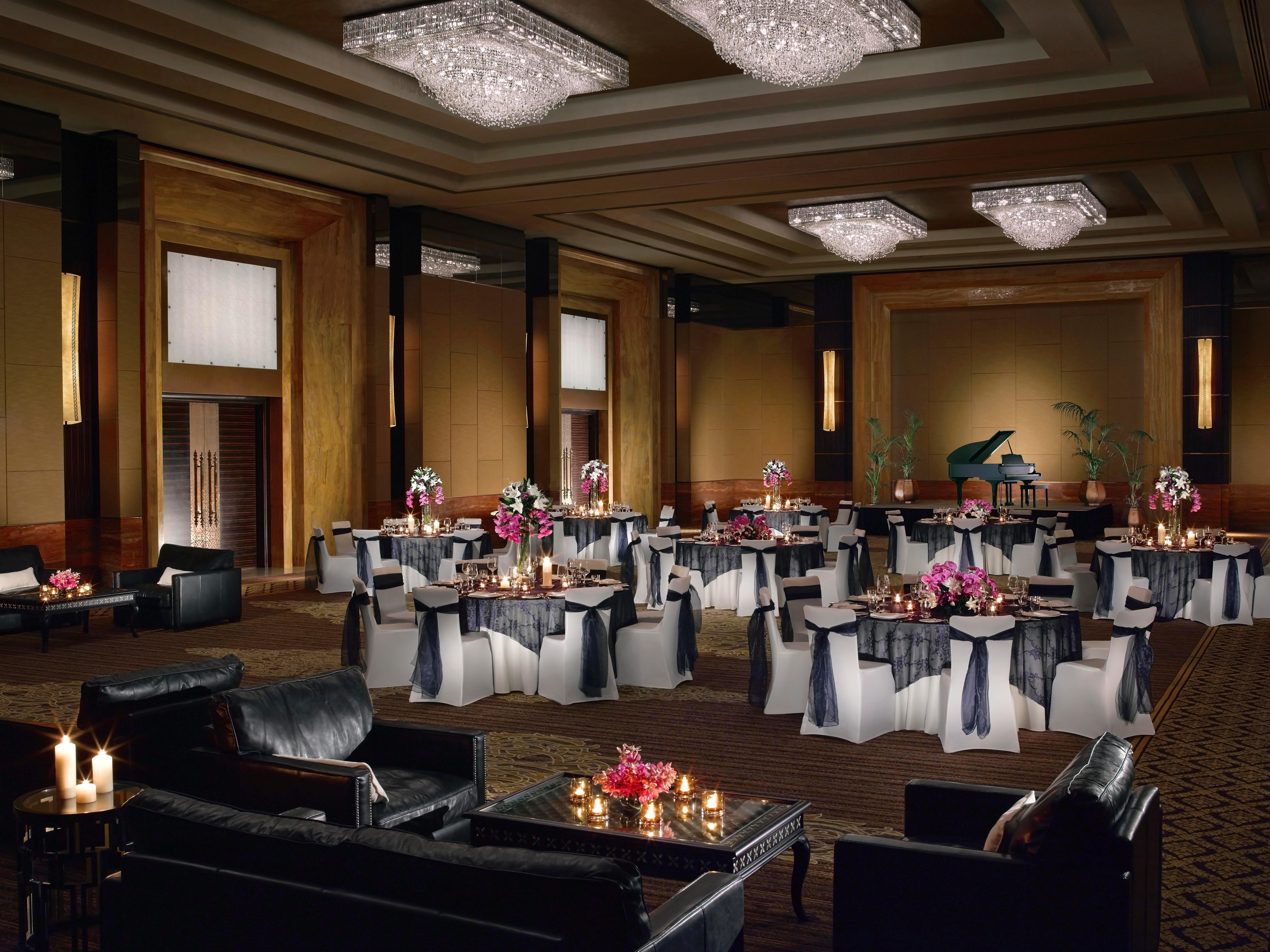 Dusit Thani Abu Dhabi Exterior photo The image shows a luxurious banquet hall or event space elegantly set up for an occasion. The room features high ceilings adorned with large, ornate chandeliers that provide warm lighting. 

Tables are arranged around the space, each covered with dar