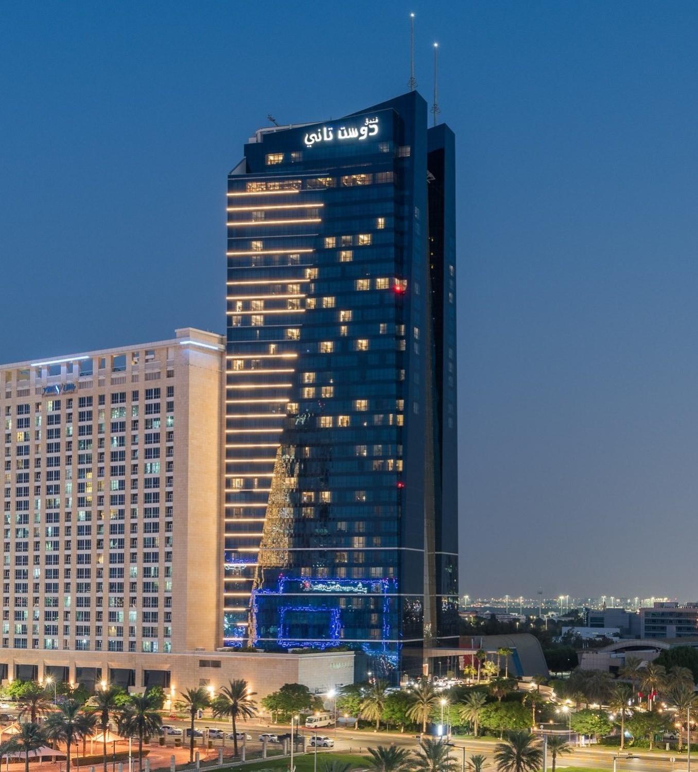 Dusit Thani Abu Dhabi Exterior photo The photo shows a modern high-rise building illuminated in the evening. The building has a sleek glass facade and features decorative lights, including a large Christmas tree design made of lights on its exterior. The structure appears to be taller t