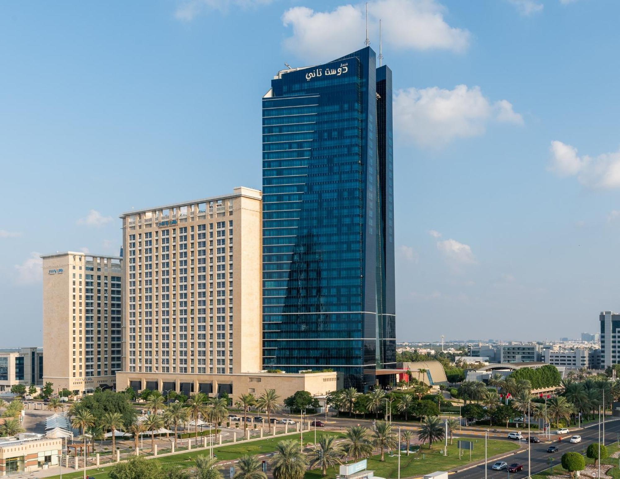 Dusit Thani Abu Dhabi Exterior photo The photo shows two modern buildings in a clear outdoor setting. The taller building on the right has a sleek, reflective glass facade and is designed with contemporary architecture, while the shorter building on the left appears to be more tradition